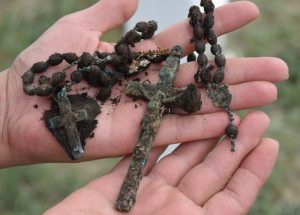 A rusted and dirt crusted rosary is displayed in outstretched hands.