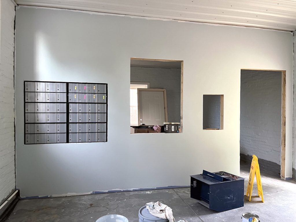 Photo of a room under construction - doors and windows are yet unframed, and two blocks of post office boxes are visible on the left side of the room.