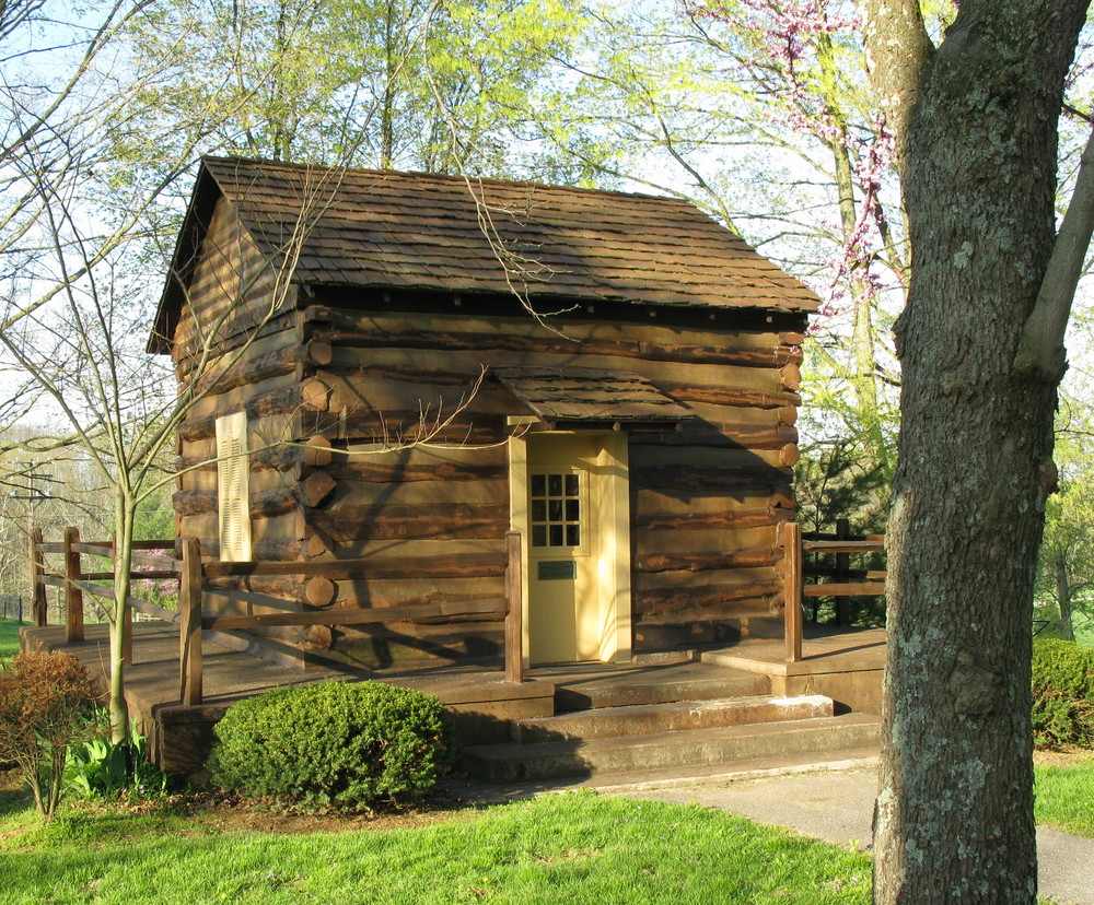 Small log cabin with yellow door and window, on a platform with a split log fence around it