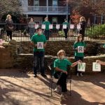 People wearing green shirts and N95 masks pose in a multilevel courtyard, holding letters that together read "WE ARE BLESSED."