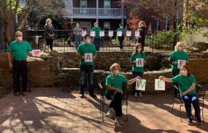 People wearing green shirts and N95 masks pose in a multilevel courtyard, holding letters that together read "WE ARE BLESSED."