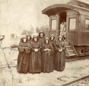 Archival photo of seven nuns in habits standing in front of a train car.