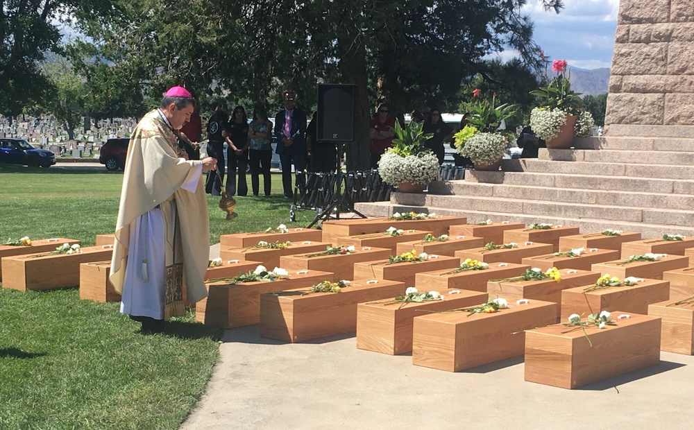 Most Rev. Jorge Rodriguez, Auxiliary Bishop of Denver, incenses rows of simple wooden caskets. 