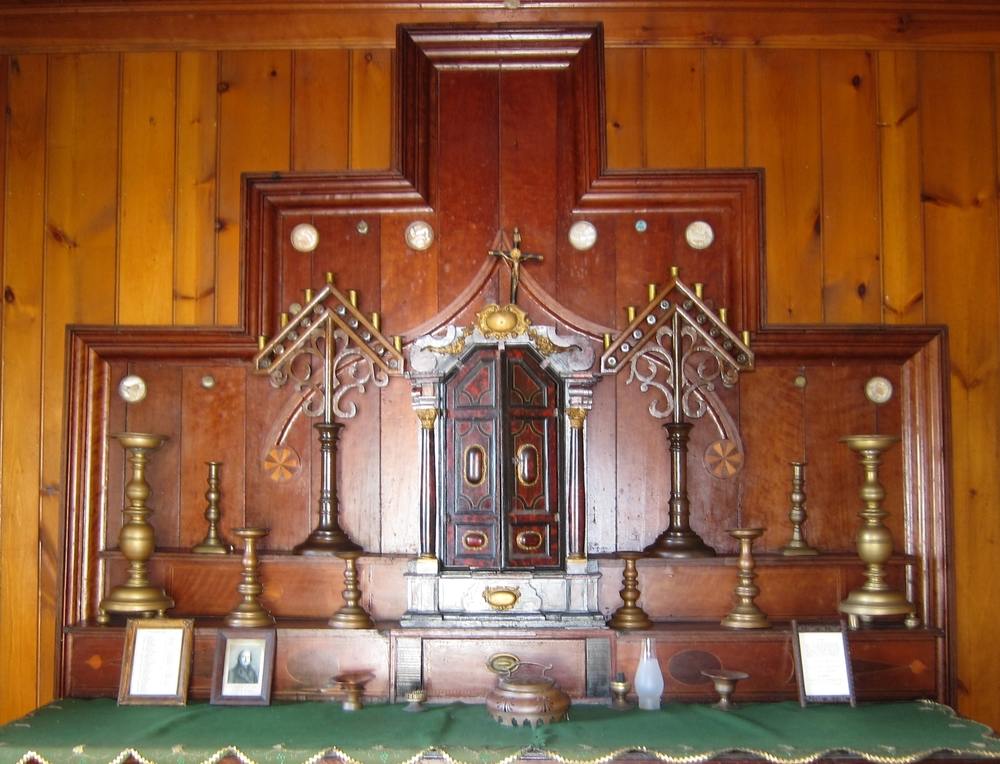 Wooden altar laid with a green and gold cloth, and with bronze and wooden candlesticks.