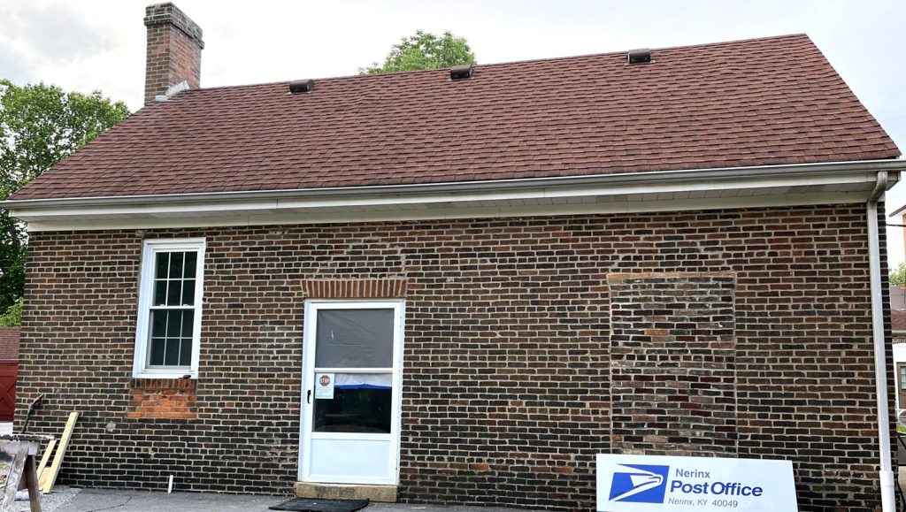 Long brick building with a sign on the ground that reads "Nerinx Post Office"