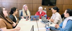 Six different women of diverse backgrounds and ages conversing happily in a discussion setting.