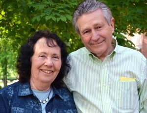 Man and women embrace one another and smile for a picture in front of green lush trees.
