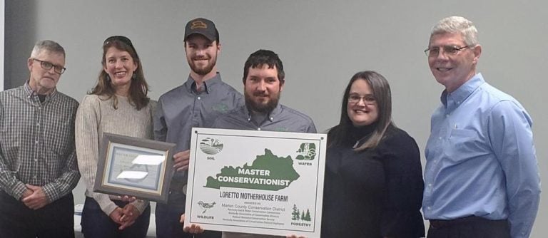 Six different individuals standing together displaying a poster and smiling for the photo.