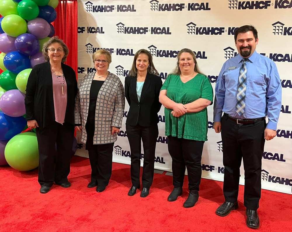 Five people stand proudly in front of an award backdrop with the text "KAHCF-KCAL" printed repeatedly.