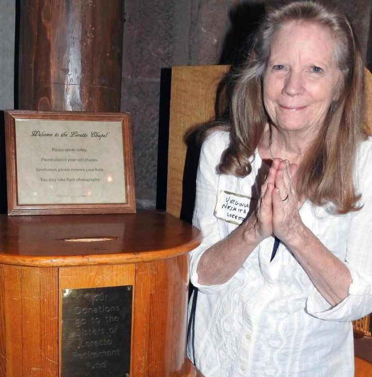 A woman with her hands clasped in gratitude in front of her stands next to a donation box in a chapel.