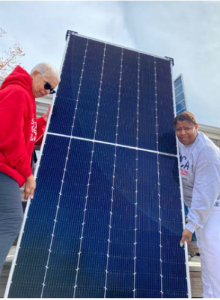 Two women, Shenandoah Valley and Monica Robinson, working together to move a large solar panel outdoors.