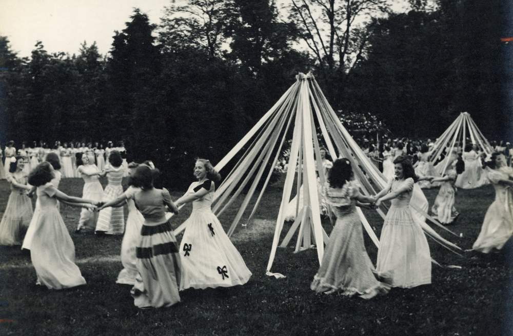 Archival photo of young women dancing around May Poles.