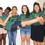 Community members posing for a photo by holding one group member horizontally across joyfully.