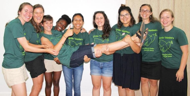 Community members posing for a photo by holding one group member horizontally across joyfully.