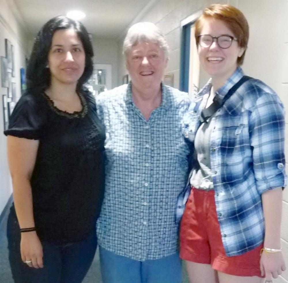 Three women standing and smiling together for a photo indoors.