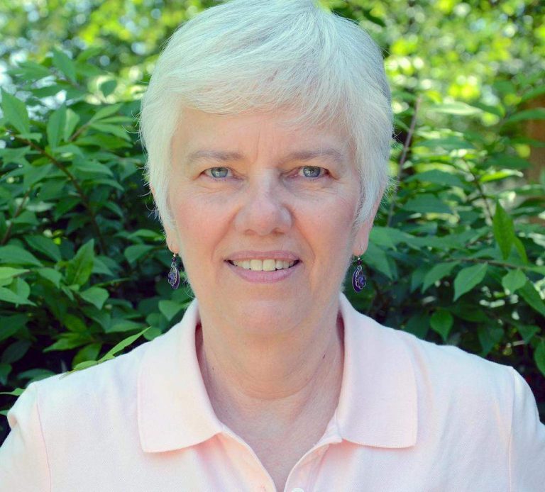Older woman smiling gleefully in front of greenery.