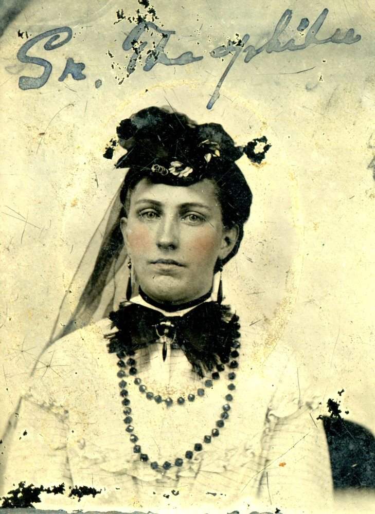 Archival portrait of a young woman wearing a hat, necklace and ornate dress.