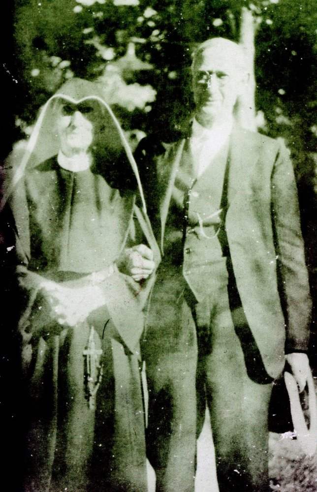 Archival photo of an elderly nun in habit standing arm and arm with an older man.