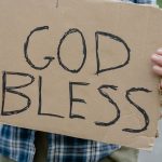 a man holding a god bless sign written on a cardboard