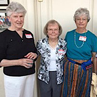 Three women standing together wearing name tags smiling for a photo indoors.