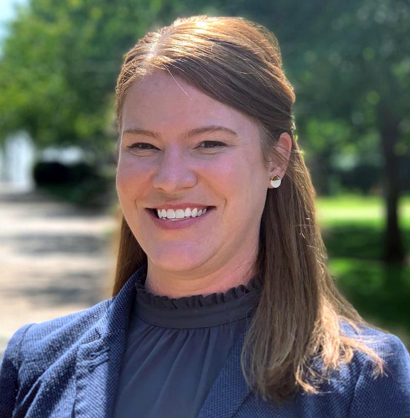 A brunette woman smiling for an outdoor portrait in a navy blouse.