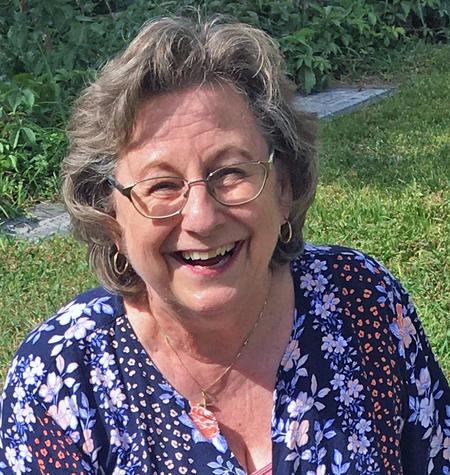 Woman in glasses smiling outdoors in a patterned blouse