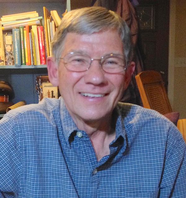 A portrait photo of a man in a collared shirt and glasses in front of a book shelf.
