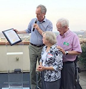Three individuals standing together presenting a plaque indoors at a ceremony.