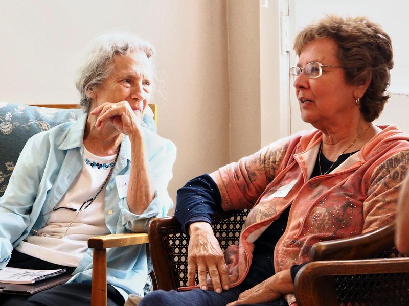 Two women lean in toward each other in conversation