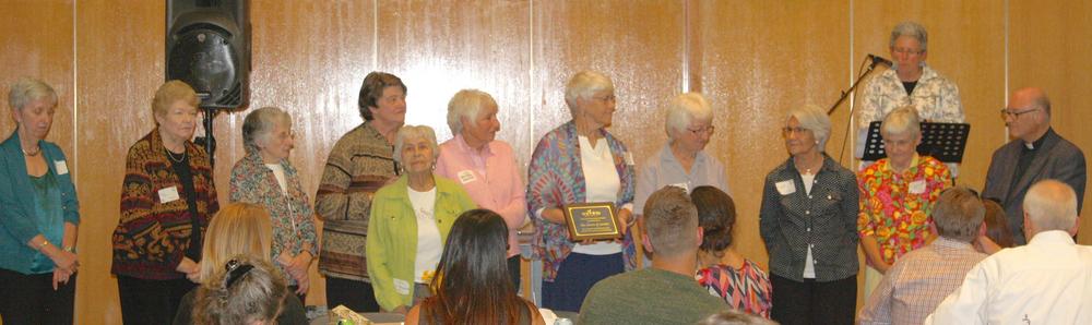 An award being presented at a ceremony with a diverse group of individuals celebrating a collective anniversary.