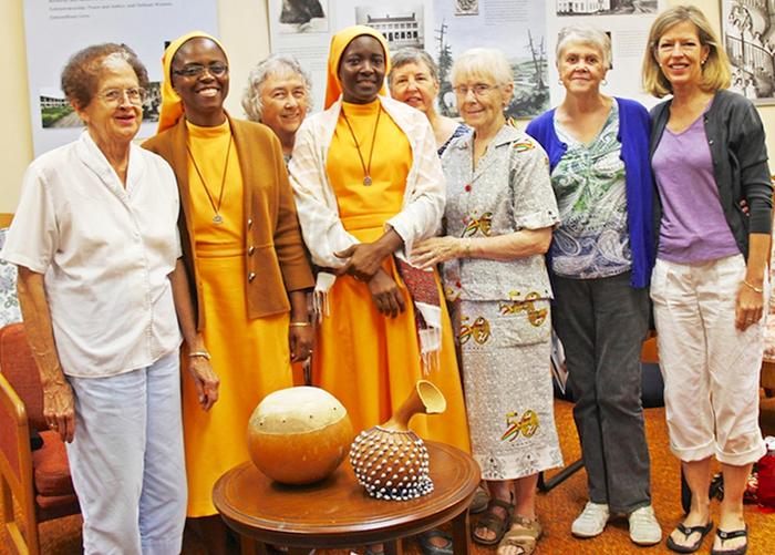 A diverse group of religious women, from Ghana and the US standing and smiling together for a photo at a committee meeting.