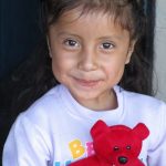Young girl smiling with a red stuffed bear in her arms.