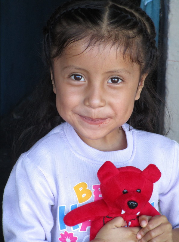 Young girl smiling with a red stuffed bear in her arms.