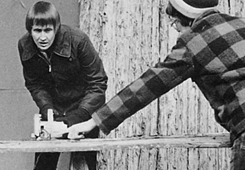 Archival black and white photo of two woman working together to saw a board.