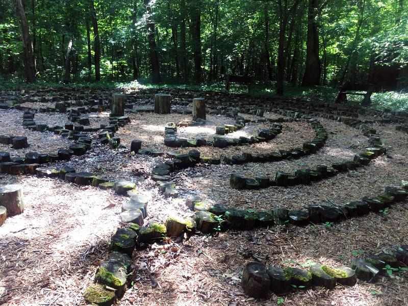 In a clearing in the woods, a labyrinth made of stones invites people to walk the mulch path.