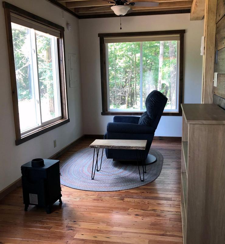 Cozy sitting room with a easy chair, table and small heater. Big windows allow light to flood the room.