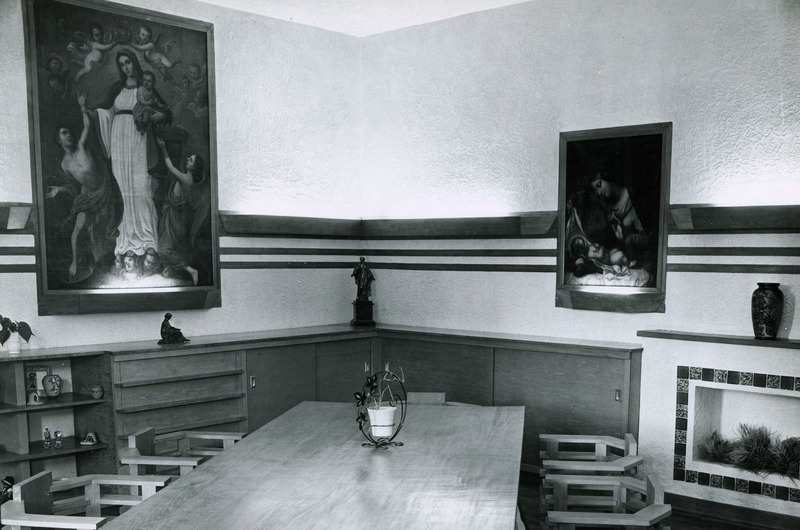 Archival photo of a meeting room with a long table surrounded by chairs. A large painting of the Virgin Mary hangs on the wall.