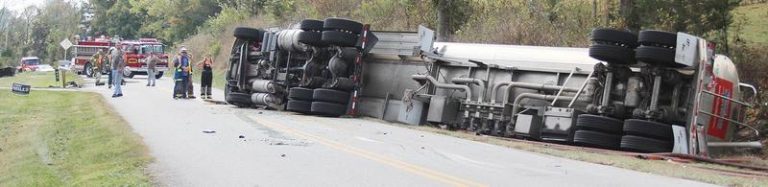 Overturned semitruck on tree lined road.