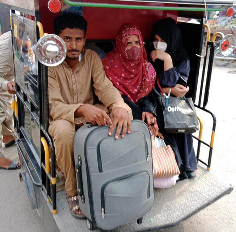 Two women wearing head scarves and masks sit with a man in the back of a bike taxi.