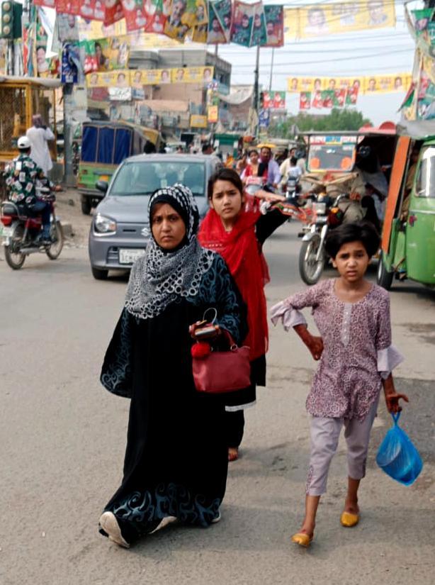 A woman with two girls walks down a busy street in Pakistan