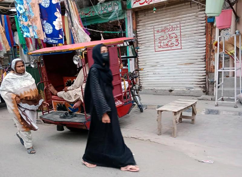 A woman dressed and wearing a black headscarf and mask walks down the street in Pakistan.
