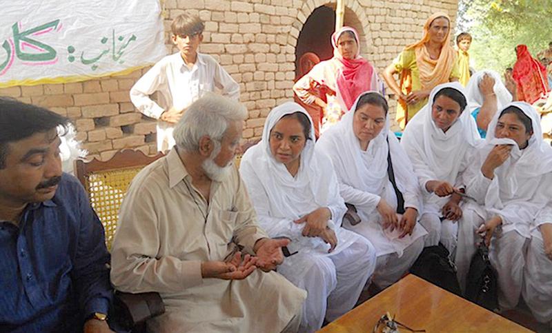 Pakistani archbishop conversing with Sisters outdoors under a shaded area.
