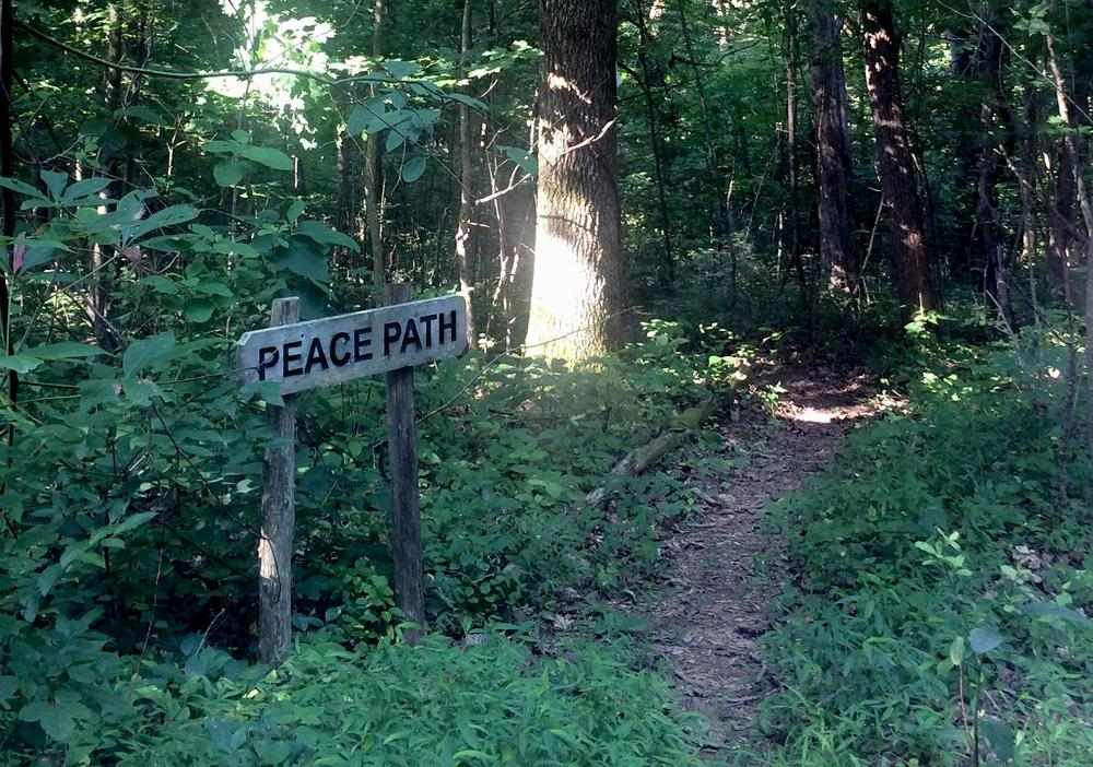 Wooden sign reading "Peace Path" marks a path leading into the woods.