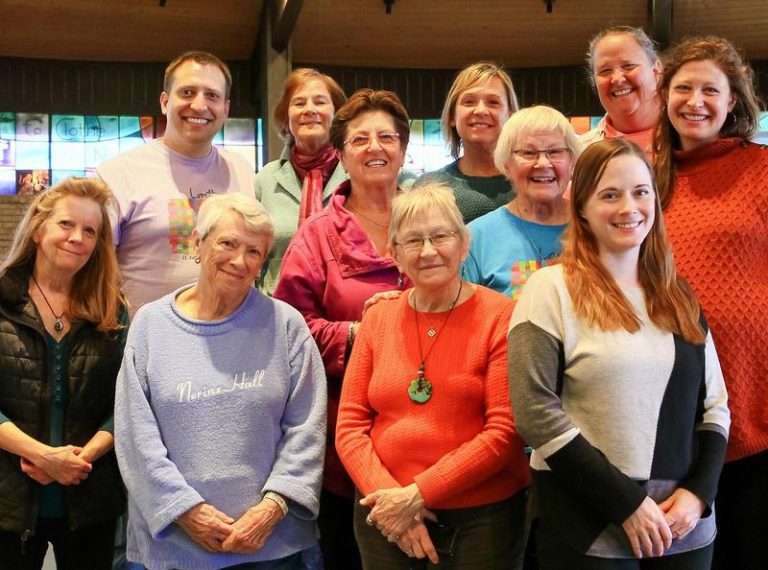 A smiling group of people, ranging in age from young adults to seniors, pose for a group photo.