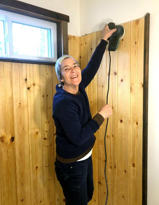 Woman holding a sander to the wall turns and smiles for the camera