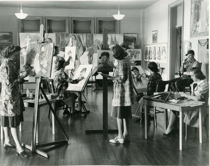 Students in an art class, standing at easels and painting portraits of a man smoking a pipe.