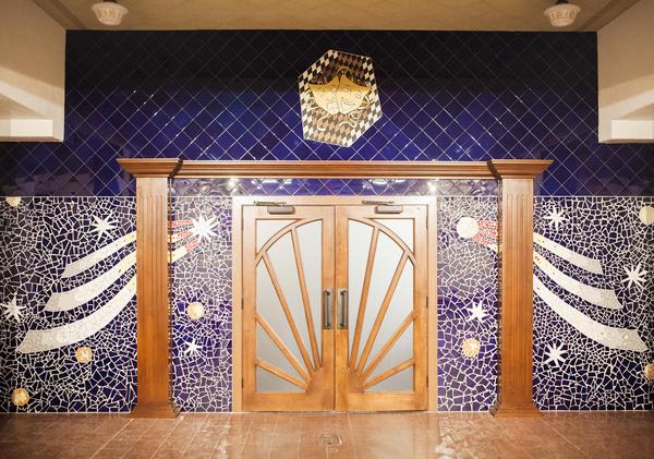 A grand theatre entrance with large wooden doors and blue mosaic detailed with shooting stars and planets.