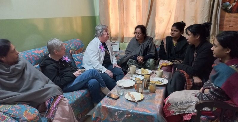 Women, some in traditional Pakistani dress, gather in a sitting room for conversation.