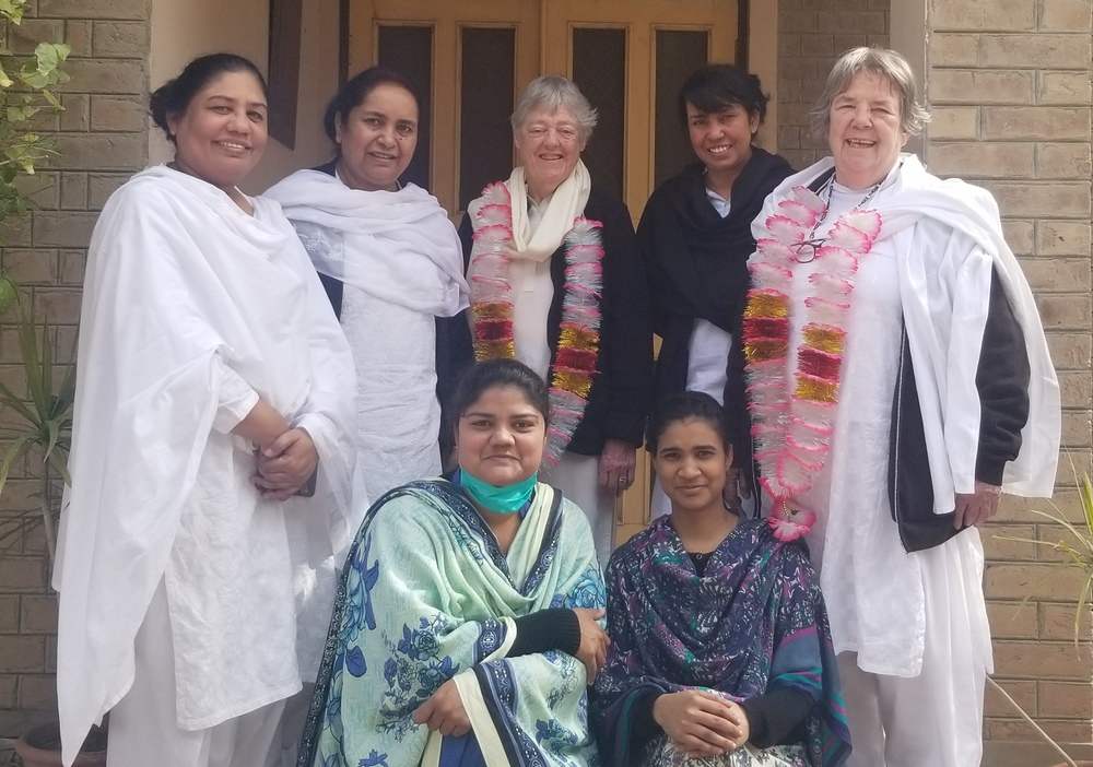 Seven women gather for a photo. Five are in white tunics and pants; two are in traditional Pakistani dress.