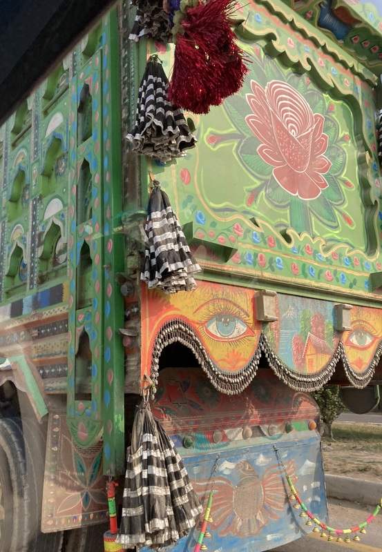 A large green truck ornately decorated with flowers, birds, and two large eyes on the back.